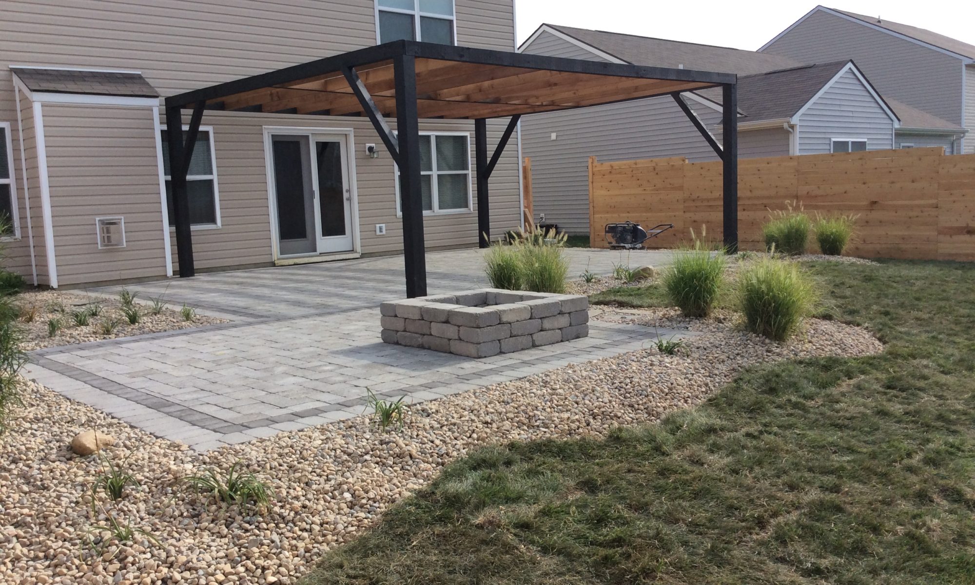 Precision Outdoors Fishers Landing Unilock Brussell block charcoal accents custom cedar pergola black matte finish rock pit install plants landscaping good burning firepit area fire pit complete property cedar slat fence custom grill island fishers indiana modern backyard