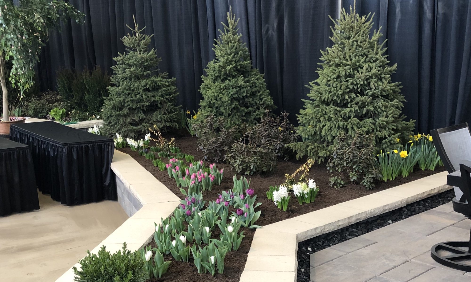 Flower and Patio Show 2019 Precision Outdoors Indianapolis Indiana sunken porcelain firepit fire pit space freestanding water wall structure cedar pergola screening walls privacy walls custom planters rough cedar pavilion gathering space outdoor kitchen grill bar space walls walkways