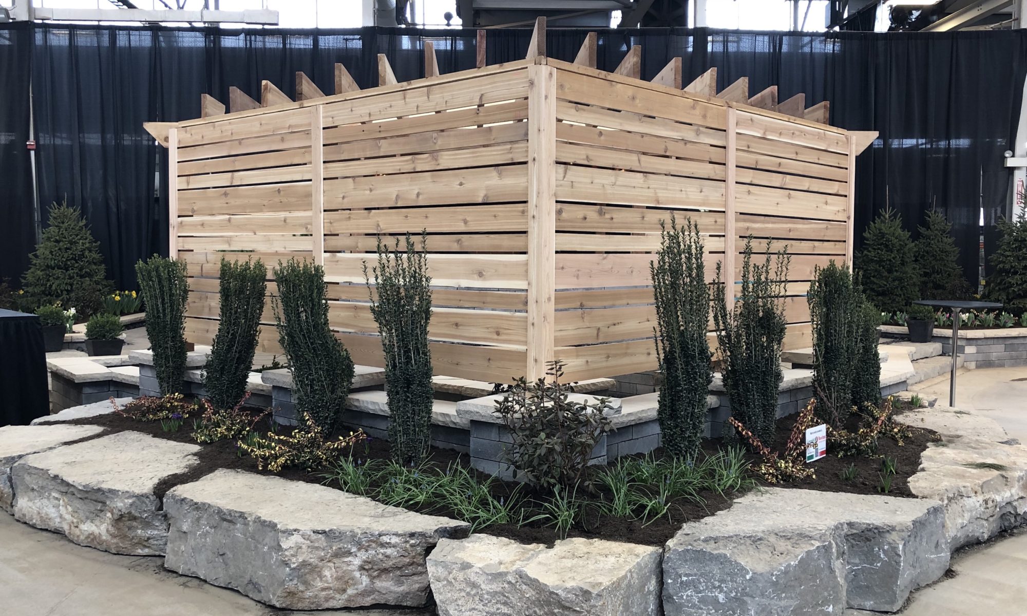 Flower and Patio Show 2019 Precision Outdoors Indianapolis Indiana sunken porcelain firepit fire pit space freestanding water wall structure cedar pergola screening walls privacy walls custom planters rough cedar pavilion gathering space outdoor kitchen grill bar space walls walkways