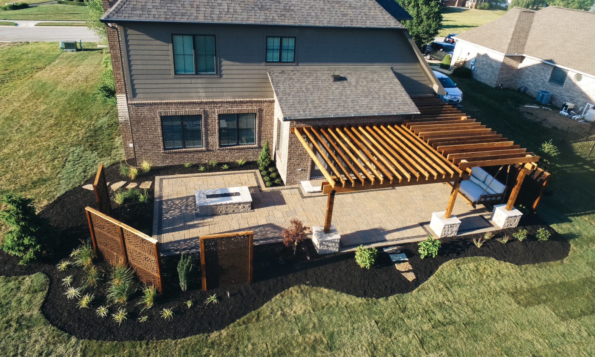 Precision Outdoors Kensington Oasis rough sawn cedar pergola black hardware decorative sunscreens outdoor gas firepit fire pit ample dining seating custom paver patio swinging daybed tech bloc semma wall sandlewood charcoal accent Carmel indiana backyard goals landscaping privacy