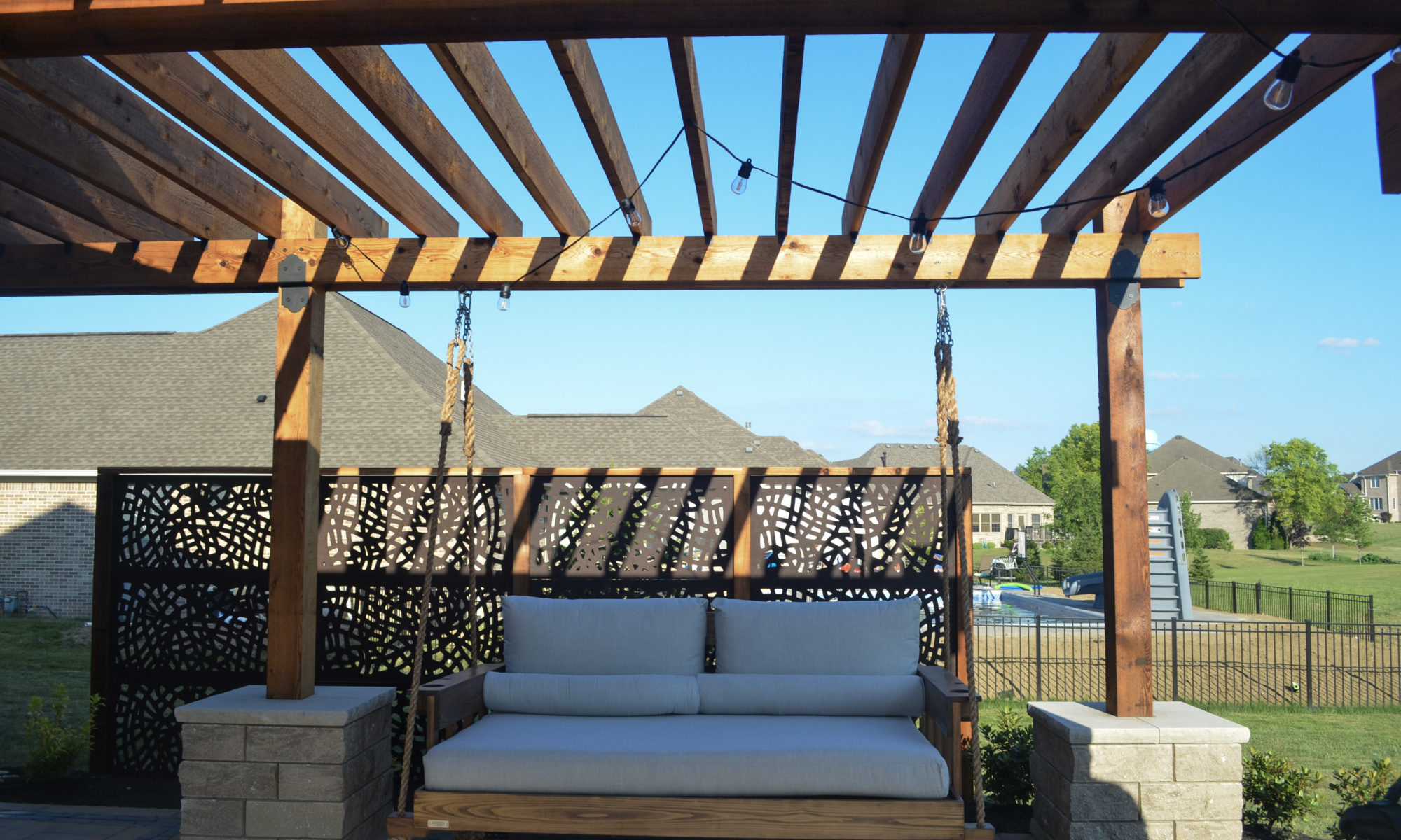 Precision Outdoors Kensington Oasis rough sawn cedar pergola black hardware decorative sunscreens outdoor gas firepit fire pit ample dining seating custom paver patio swinging daybed tech bloc semma wall sandlewood charcoal accent Carmel indiana backyard goals landscaping privacy