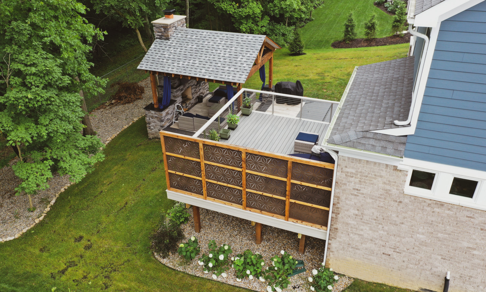 Gable Roof Structure Wood Burning Fireplace with gas fire log starter Outdoor Living by Belgard Noon tile patio Raised Deck Modern cable railing Privacy screens