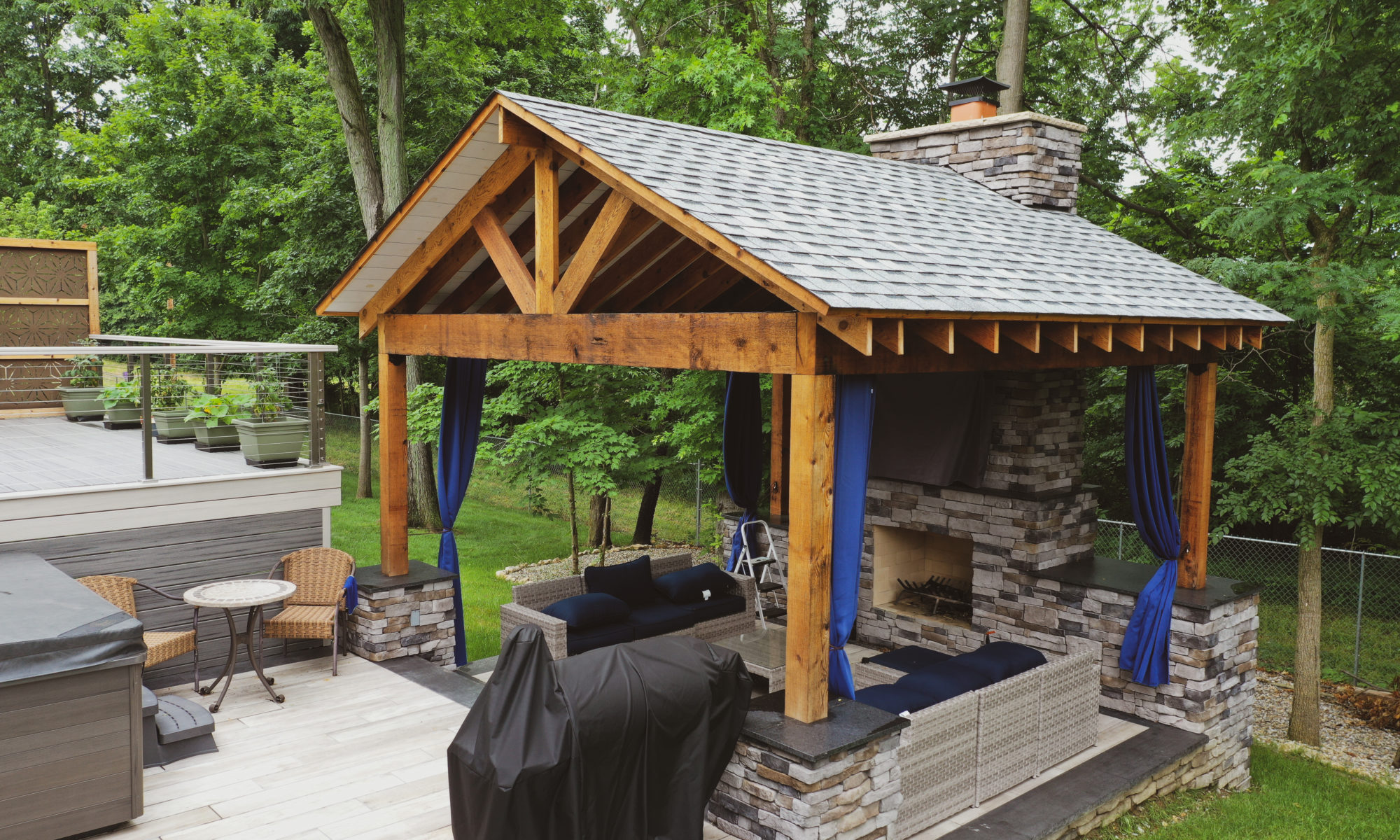 Gable Roof Structure Wood Burning Fireplace with gas fire log starter Outdoor Living by Belgard Noon tile patio Raised Deck Modern cable railing Privacy screens