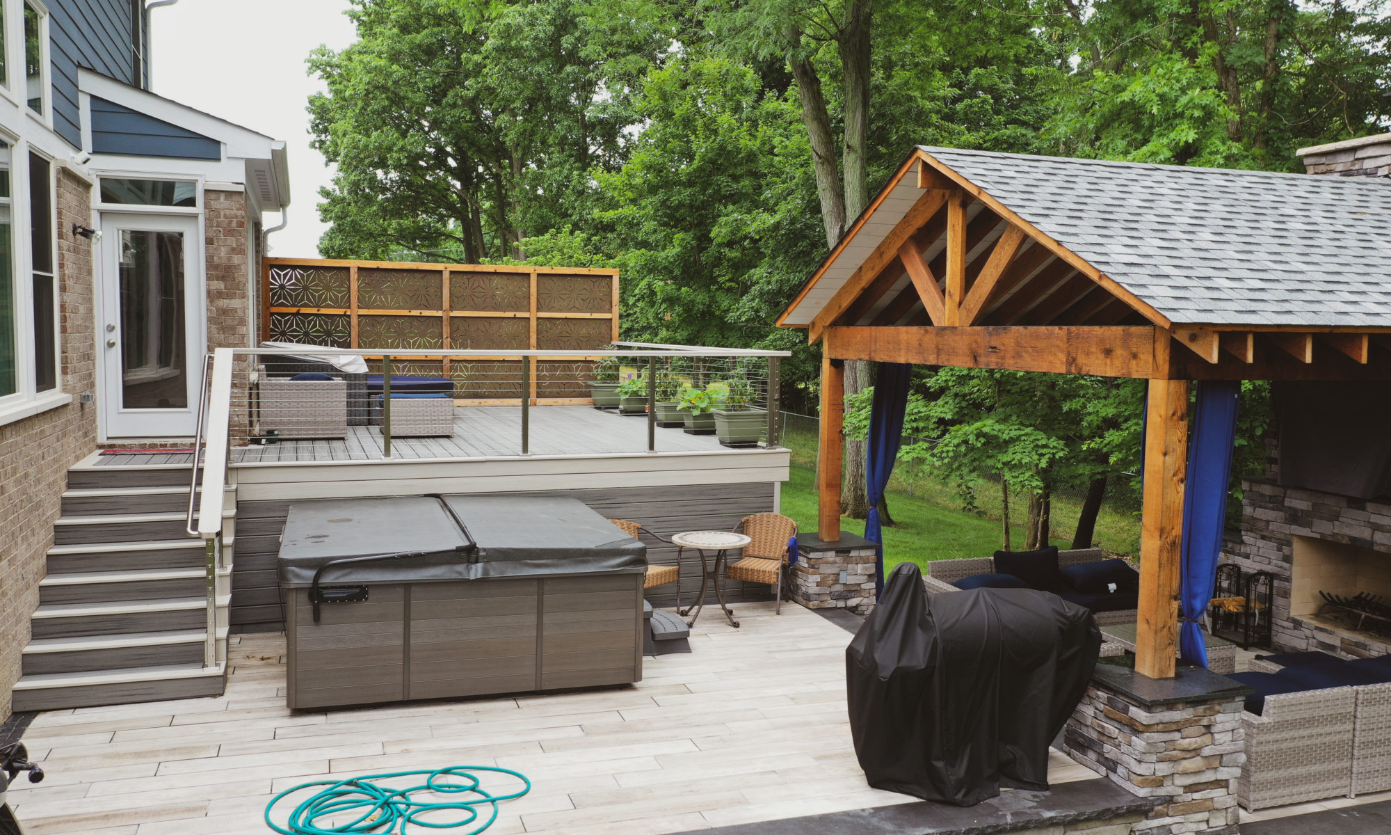 Gable Roof Structure Wood Burning Fireplace with gas fire log starter Outdoor Living by Belgard Noon tile patio Raised Deck Modern cable railing Privacy screens