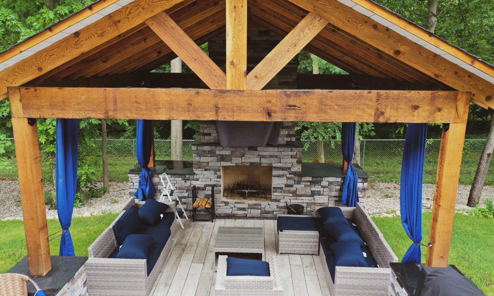 Gable Roof Structure Wood Burning Fireplace with gas fire log starter Outdoor Living by Belgard Noon tile patio Raised Deck Modern cable railing Privacy screens