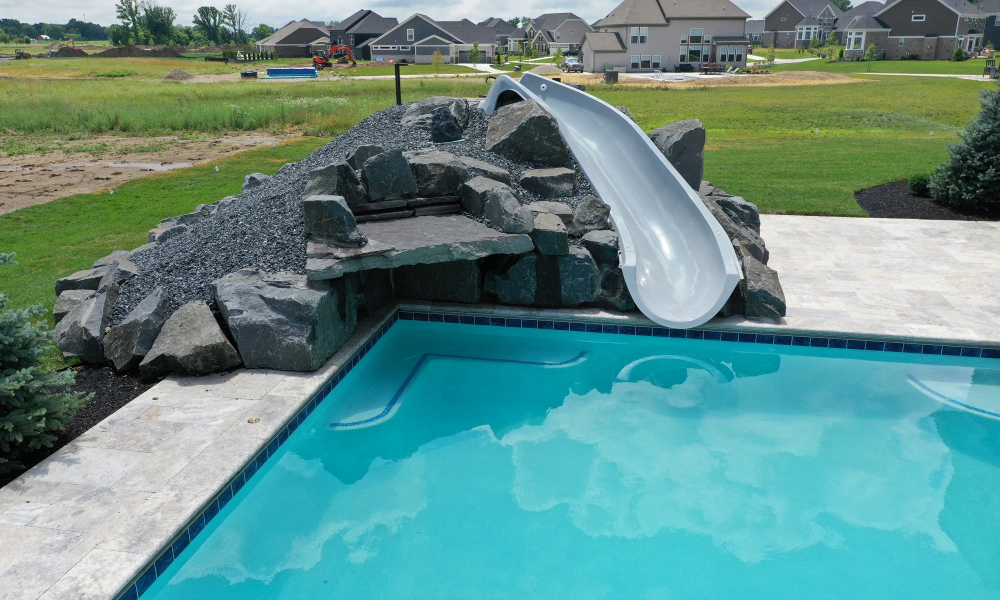poolside pavillion paver patio pool fire fireplace stairs cover gray grey tanning deck graven plants trees flowers black