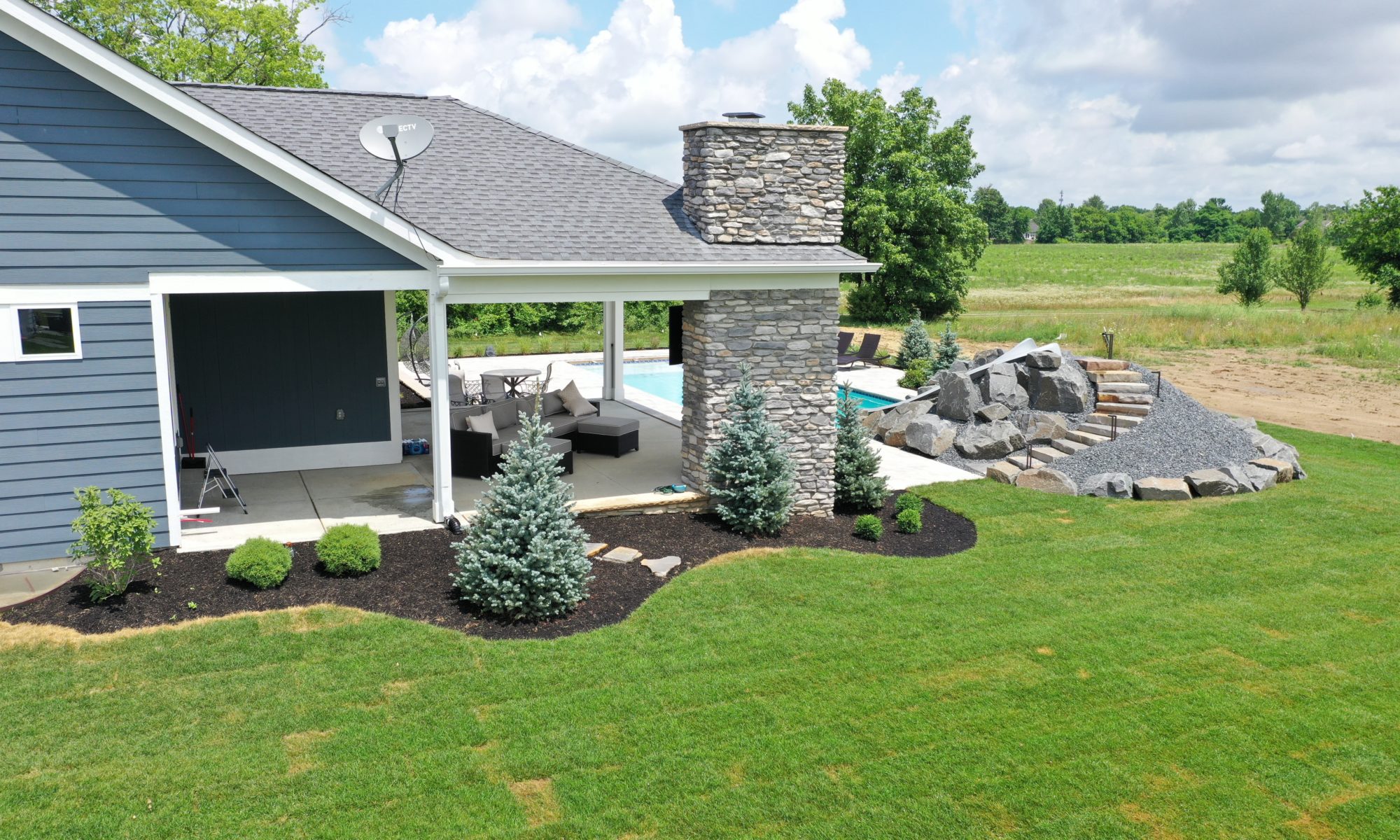 poolside pavilion paver patio pool fire fireplace stairs cover gray grey tanning deck graven plants trees flowers black
