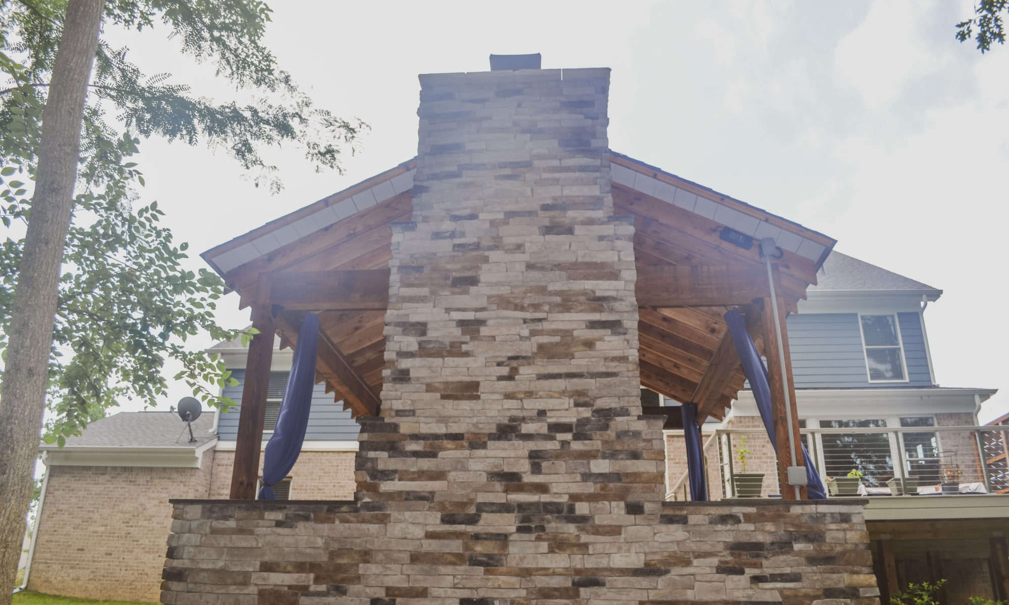Gable Roof Structure Wood Burning Fireplace with gas fire log starter Outdoor Living by Belgard Noon tile patio Raised Deck Modern cable railing Privacy screens