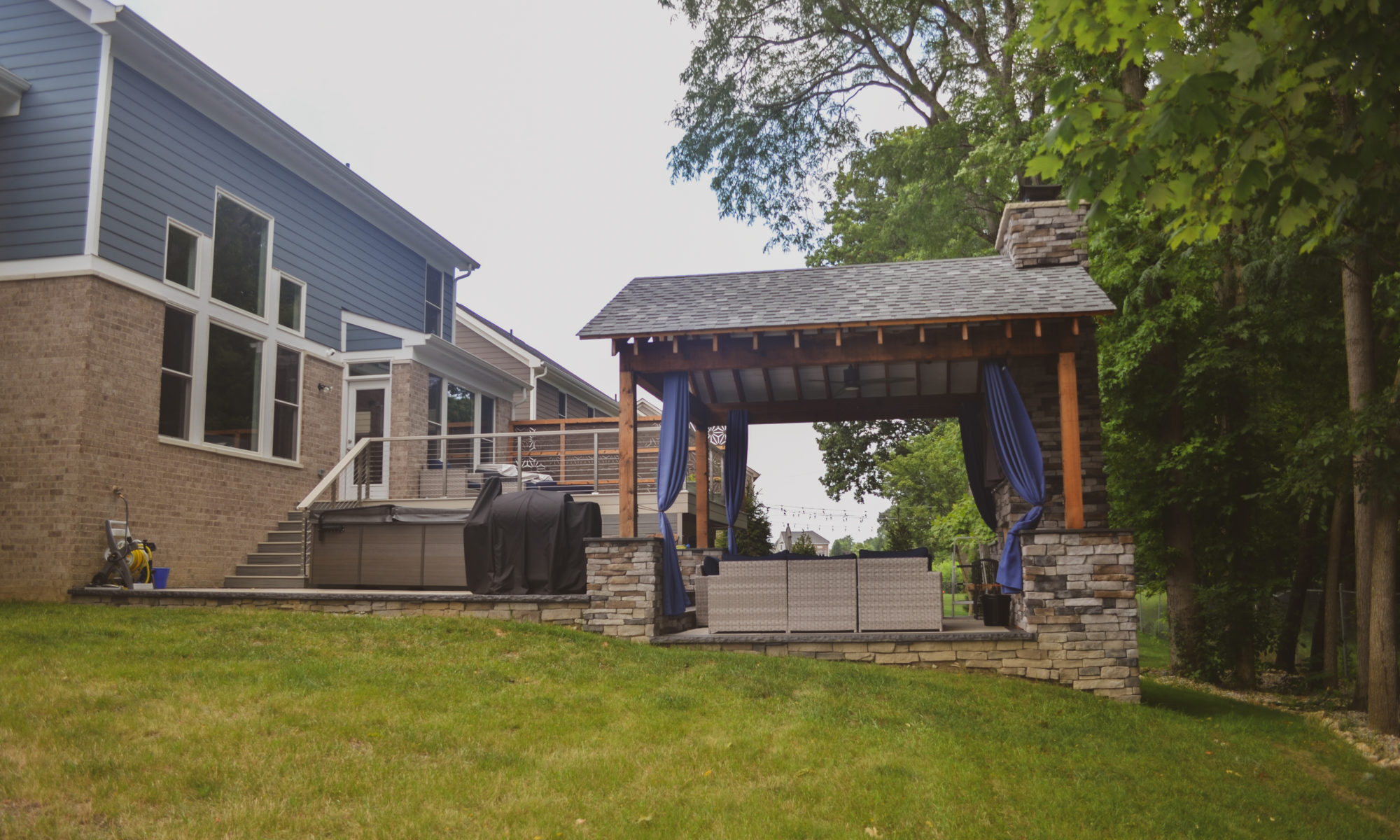 Gable Roof Structure Wood Burning Fireplace with gas fire log starter Outdoor Living by Belgard Noon tile patio Raised Deck Modern cable railing Privacy screens