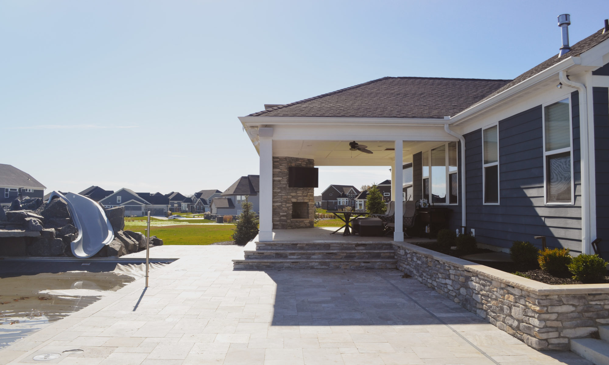 poolside pavillion paver patio pool fire fireplace stairs cover gray grey tanning deck graven plants trees flowers black