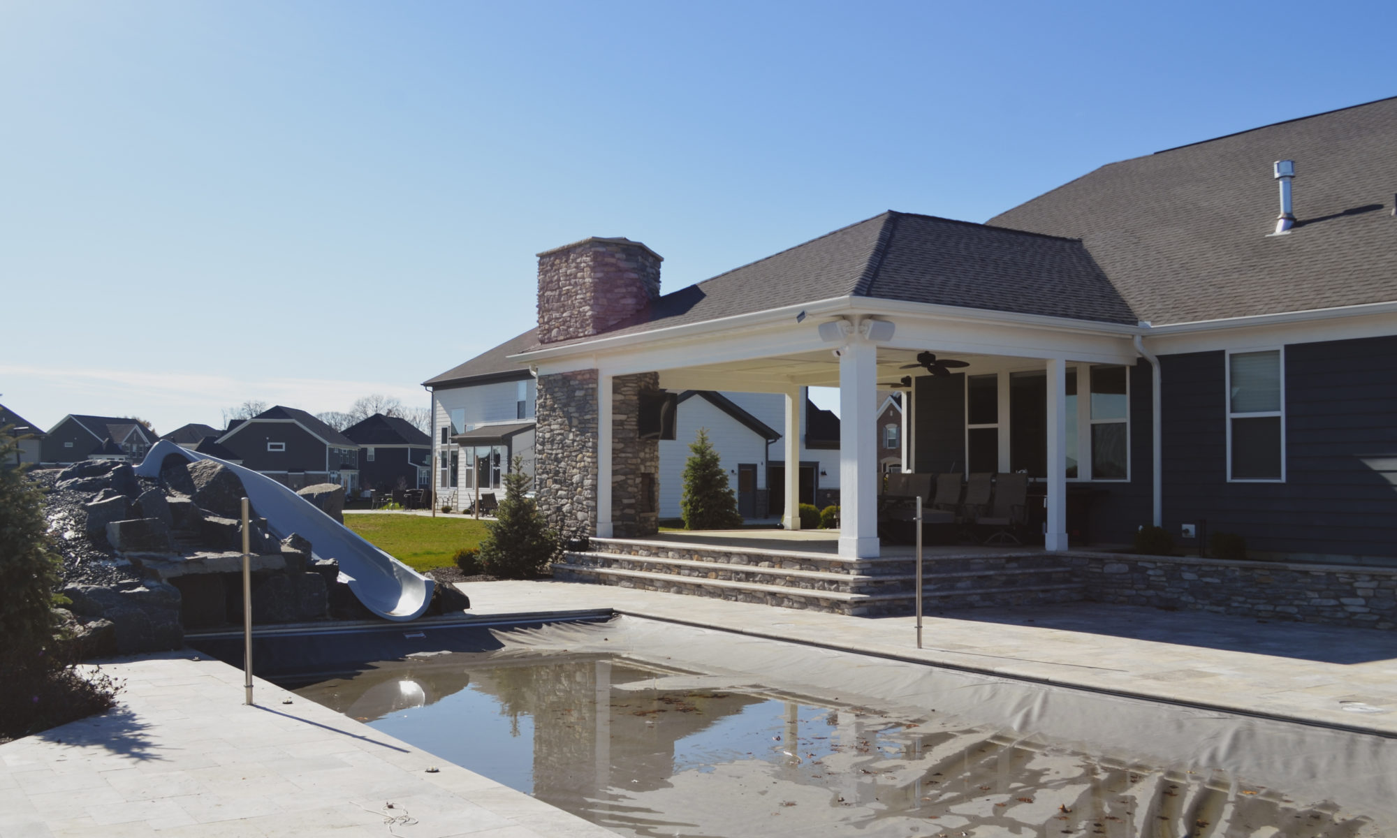 poolside pavillion paver patio pool fire fireplace stairs cover gray grey tanning deck graven plants trees flowers black