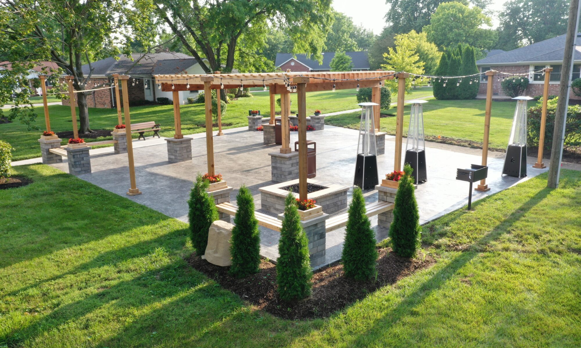 Precision Outdoors Greenwood Indiana Smock Courtyard senior living community large pergola arborvitae bubbling boulder water feature fountain propane fire pit seating corner propane heaters heat source custom landscaping flowers mulch night lighting string lights grill propane heaters flowers shared living space exterior design and build perfectly manicured turf